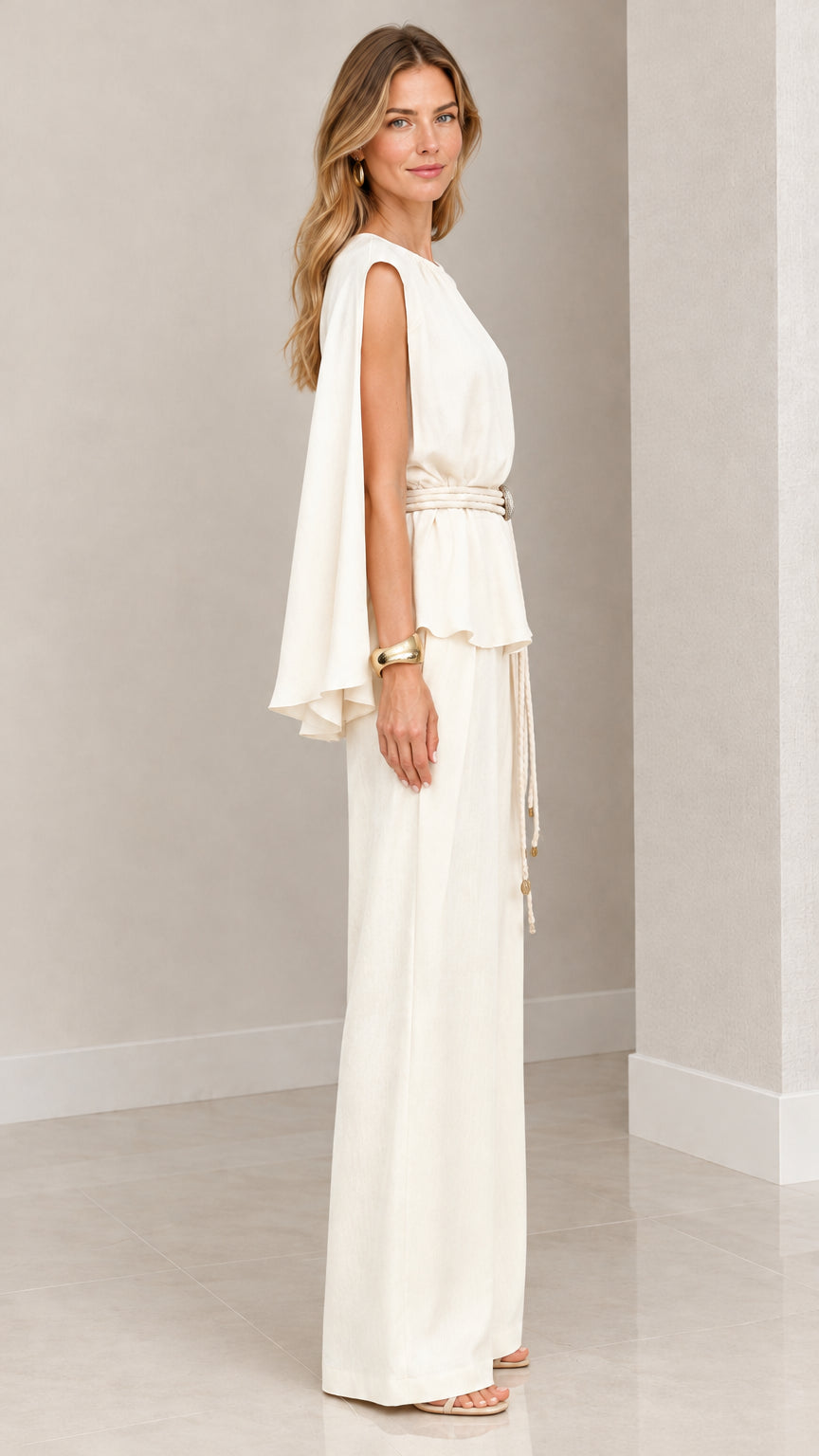 Side angle view of woman wearing cream cape sleeve top and wide leg trousers