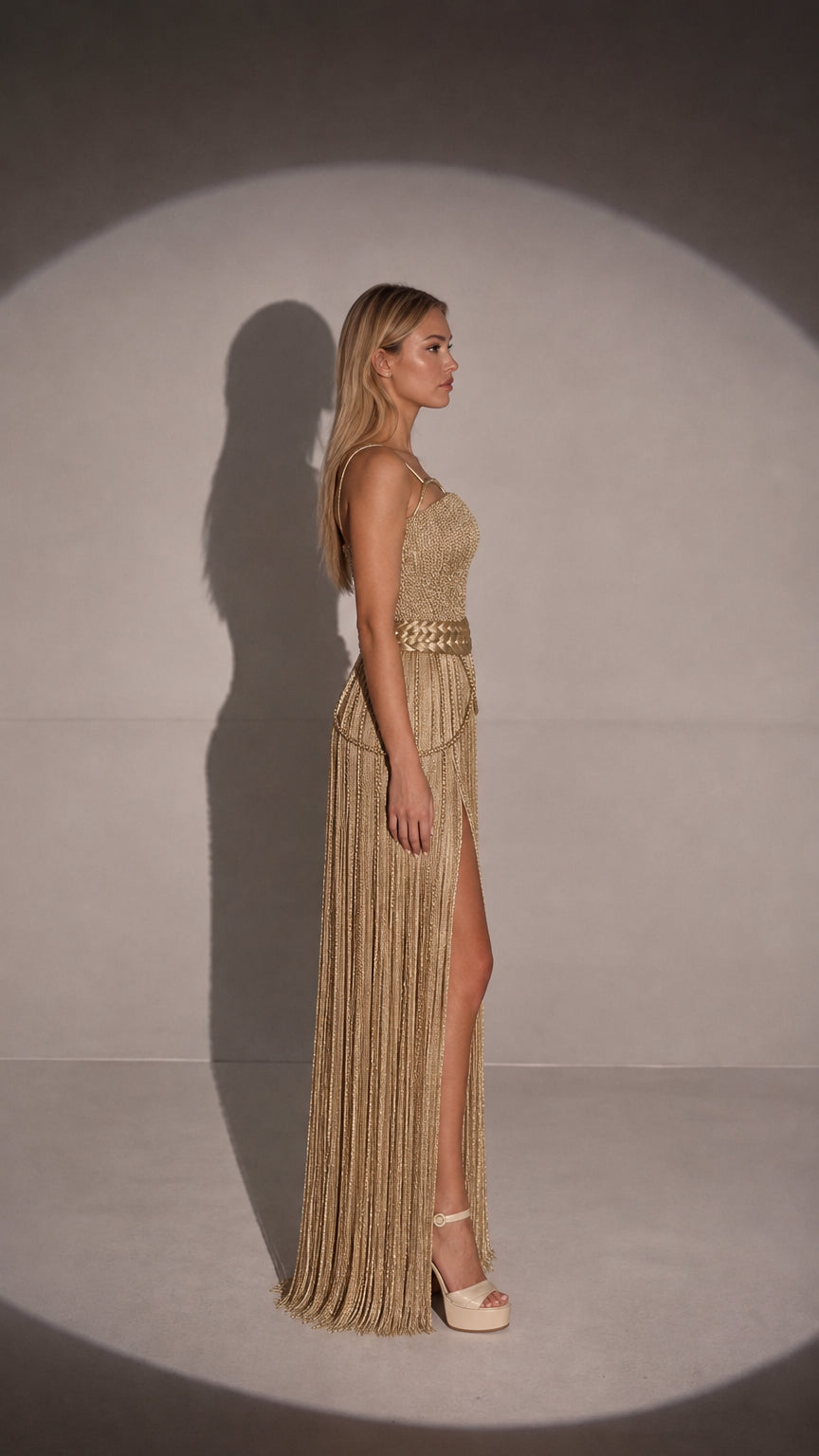 Side profile view of gold one-shoulder fringe evening dress with slit