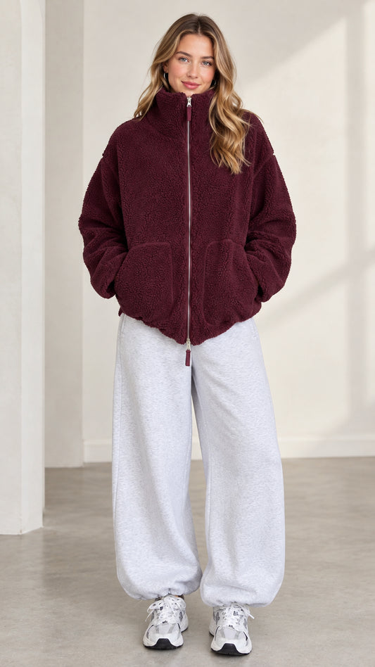 Front view of model wearing burgundy zip-up teddy fleece jacket and grey sweatpants