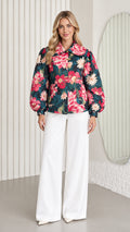 Front full-length view of model wearing dark teal floral jacket with balloon sleeves and white wide-leg trousers