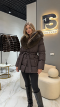 Front view of model wearing chocolate brown belted puffer coat with plush faux fur collar