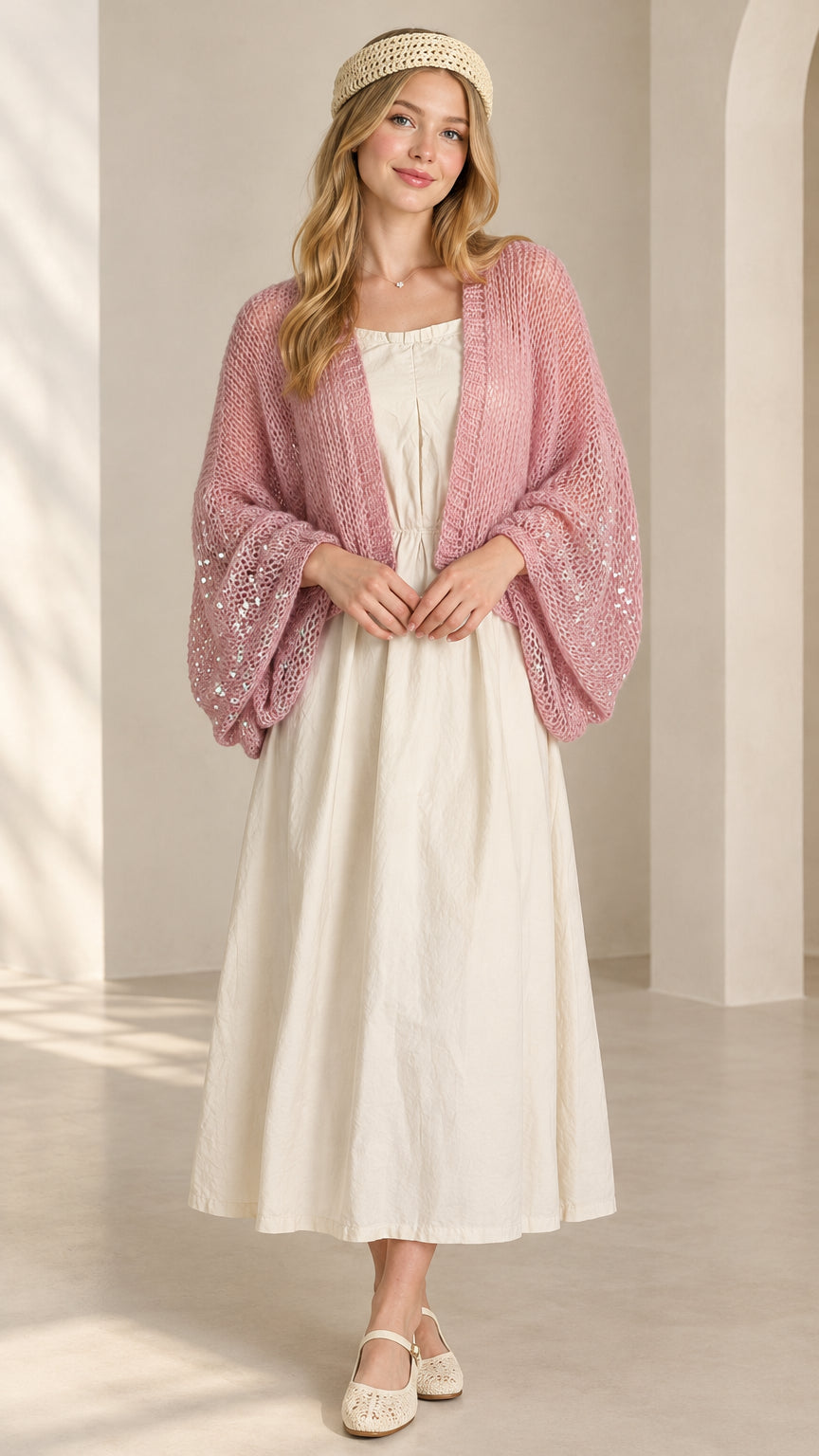 Front view of woman wearing pink sequin open-knit shrug over cream maxi dress