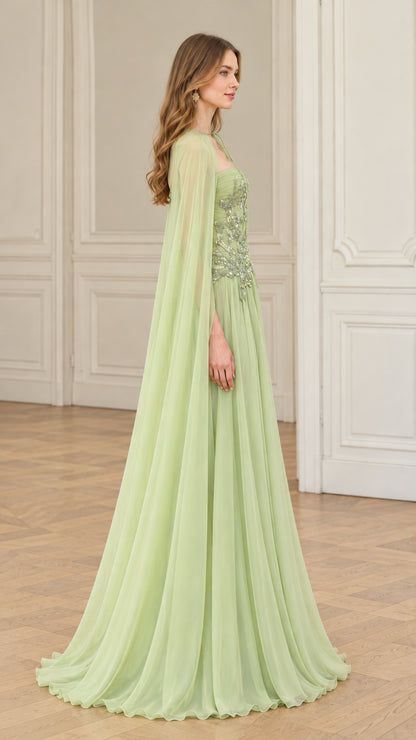 Side profile of sage green embellished formal gown with flowing floor-length cape