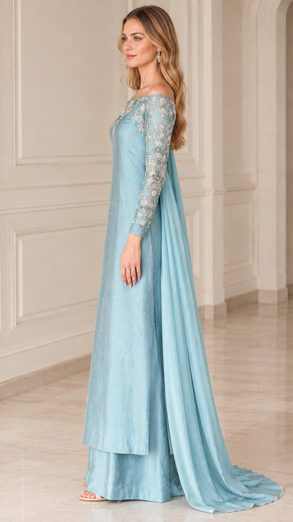 Side profile view of dusty blue formal gown ensemble showcasing layered maxi skirt and cape drape