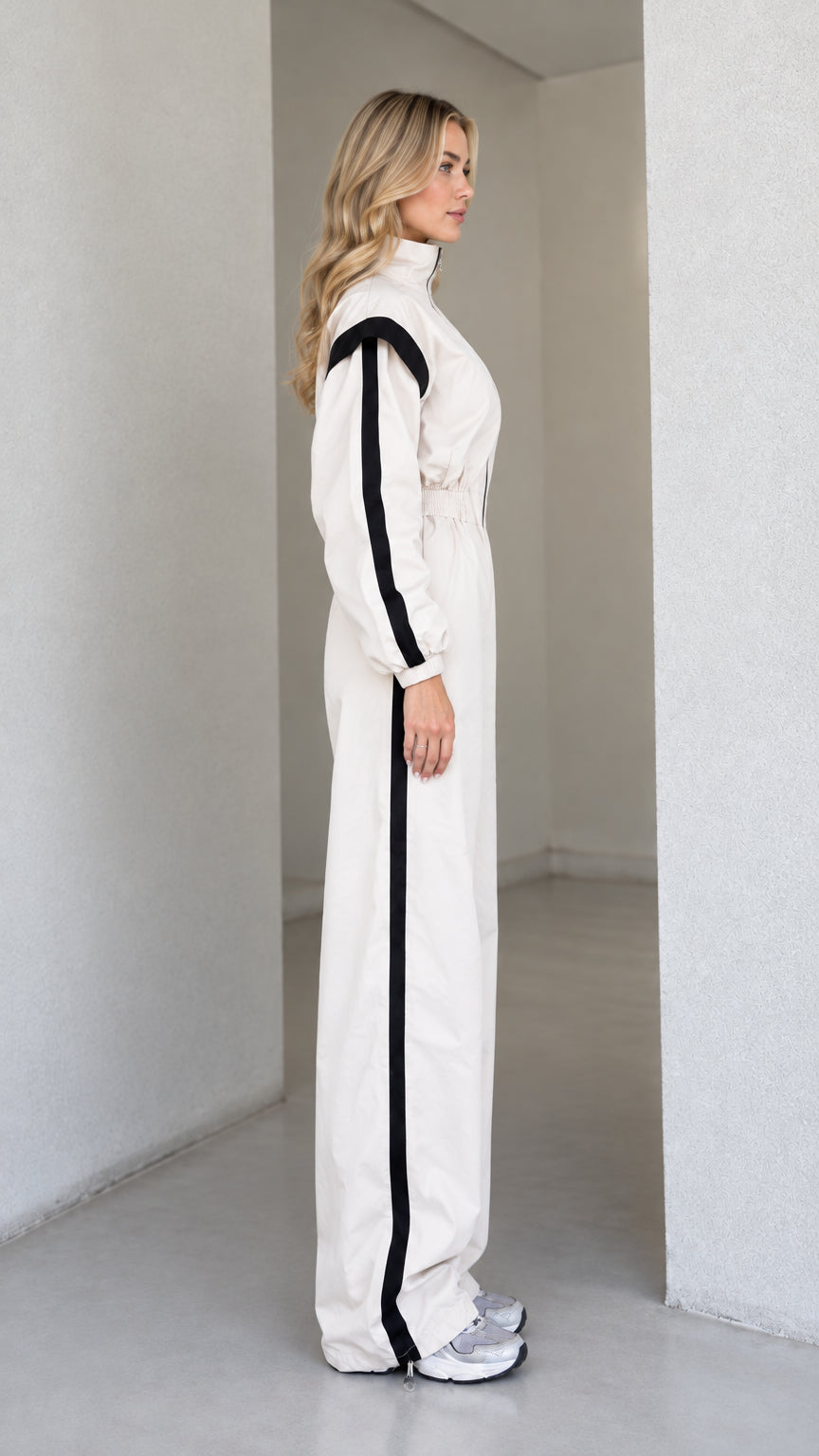 Side profile view of women's cream zip-front track jumpsuit