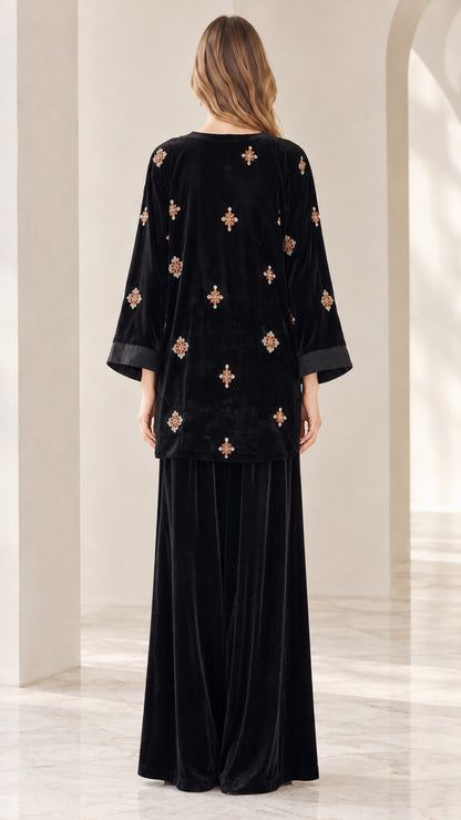 Back view of model wearing black velvet embroidered tunic top and wide leg pants