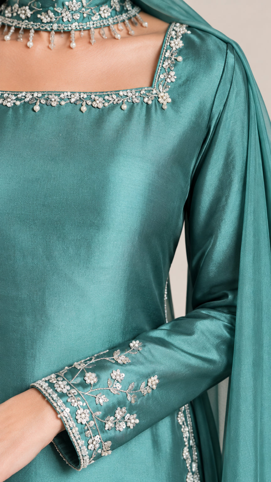 Close-up detail of silver embroidery, beaded trim, and neckline on teal fabric
