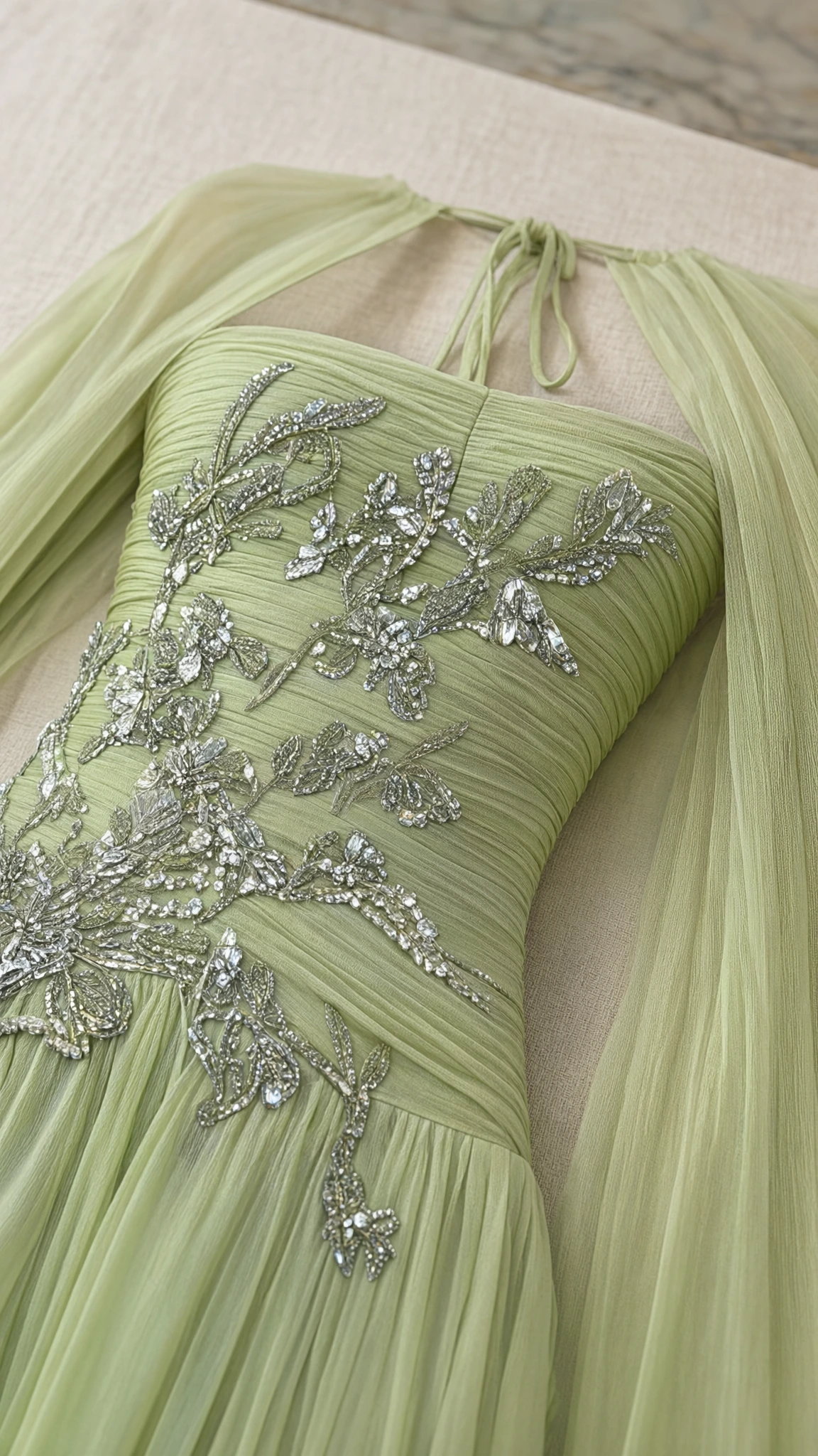 Close-up detail of silver floral beadwork and pleating on sage green gown bodice