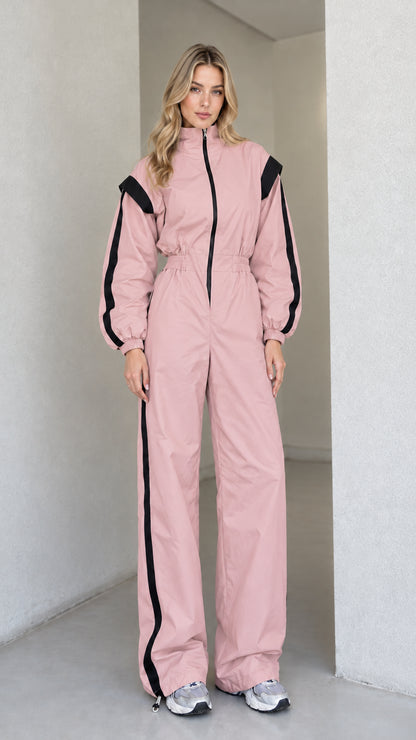 Full front view of women's dusty pink track jumpsuit with black side stripes