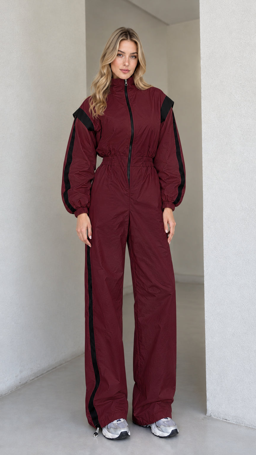 Full front view of women's burgundy track jumpsuit with black side stripes